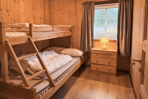 Hyggeligt soverum i træ med køjeseng, kommode, vindue og varme farver på Trollhytta-lodgen i Danmark.
