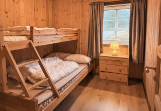Hyggeligt soverum i træ med køjeseng, kommode, vindue og varme farver på Trollhytta-lodgen i Danmark.