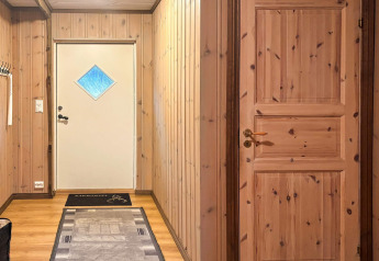 Entrée du lodge '76409 TROLLHYTTA' au Danemark avec murs en bois, porte blanche et tapis au sol.