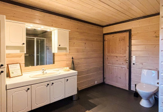 Badeværelse i lodge 76409 TROLLHYTTA i Danmark med træpaneler, hvidt skab, spejl og moderne toilet.
