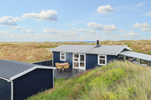'Seaside Bliss in albaek' lodge tussen Deense duinen, met blauwe lucht en zicht op zee op de achtergrond.