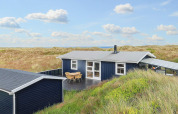Sort sommerhus kaldet 'Seaside Bliss in albaek' beliggende i klitterne ved den danske kyst under en klar himmel.