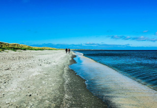Bred sandstrand og klart blåt hav ved Seaside Bliss i albaek, Danmark, med folk der går langs vandet.