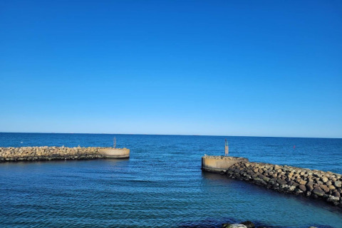Udsigt fra Seaside Bliss i Albaek, Danmark, med klare blå himmel og stenmoler ved havet.