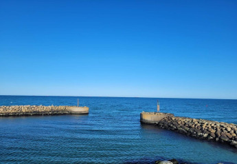 Udsigt fra Seaside Bliss i Albaek, Danmark, med klare blå himmel og stenmoler ved havet.