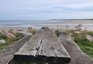 Tavolo e panca di legno sulla spiaggia a Seaside Bliss in Albaek, Danimarca, con vista su mare e cielo.