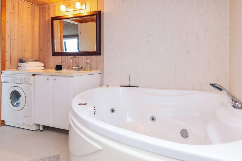 Moderne badeværelse i «Seaside Bliss in Albaek» med rund jacuzzi, vaskemaskine og træpaneler i Danmark.