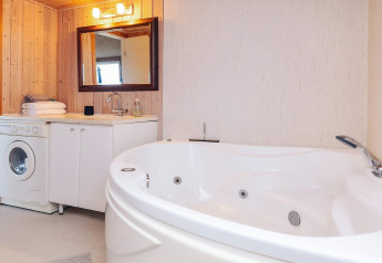 Moderne badeværelse i «Seaside Bliss in Albaek» med rund jacuzzi, vaskemaskine og træpaneler i Danmark.
