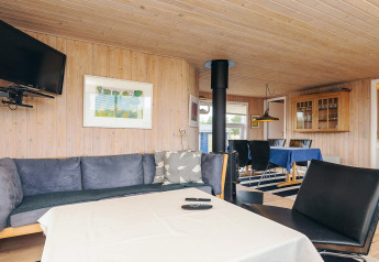 Living room with wood walls, black sofa, dining table, and TV at Seaside Bliss in Albaek, Denmark.