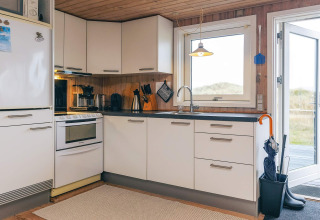 Moderne keuken in Seaside Bliss in Albaek, Denemarken; witte kastjes en uitzicht naar buiten.
