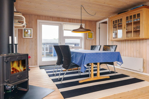 Comedor en la cabaña Seaside Bliss en Albaek, Dinamarca, con estufa de leña, mantel azul y alfombra rayada.