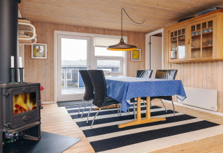 Spisestue i hytten Seaside Bliss i Albaek, Danmark, med brændeovn, sort-hvide tæpper og blå dug.