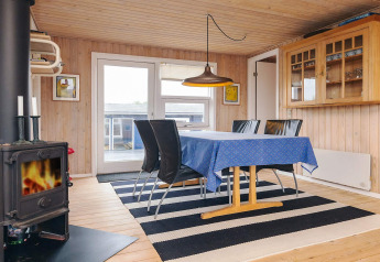 Salle à manger du lodge Seaside Bliss à Albaek, Danemark, avec poêle, nappe bleue et tapis rayé.