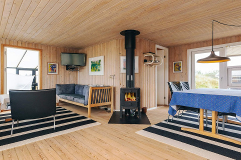 Intérieur lumineux du lodge Seaside Bliss à Albaek, Danemark, avec poêle, canapé et table à manger.
