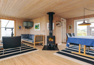 Intérieur lumineux du lodge Seaside Bliss à Albaek, Danemark, avec poêle, canapé et table à manger.