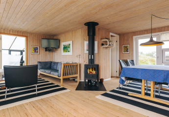 Lyst interiør i Seaside Bliss i Albaek, Danmark, med brændeovn, sofa, spisebord og vægkunst.