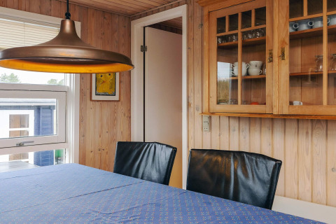 Spiseområde i Seaside Bliss i Albaek, Danmark, med trævægge, glasvitrine og moderne lamper.