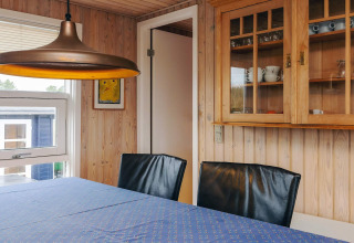 Essbereich in Seaside Bliss in Albaek, Dänemark, mit Holzwänden, Glasschrank und moderner Lampe.