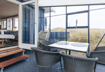 Seaside Bliss lodge in Albaek, Denmark: cozy patio with dining set, chairs and scenic dune landscape view.