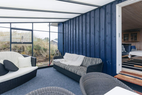 Veranda luminosa con parete in legno blu, sedute comode e vista natura al Seaside Bliss di Albaek, Danimarca.