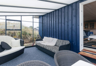 Soleada terraza acristalada con pared azul, cómodos asientos y vista natural en Seaside Bliss de Albaek, Dinamarca.