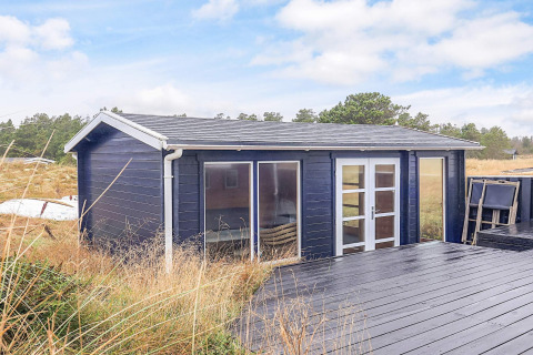 Kleine dunkelblaue Holzhütte bei Seaside Bliss in Albaek, Dänemark, mit Terrasse und Natur umgeben.