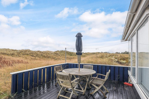 Terraza de madera con sillas exteriores y paraguas cerrado en Seaside Bliss en Albaek, Dinamarca.