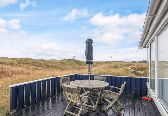 Wooden terrace with outdoor chairs and a closed umbrella at Seaside Bliss in Albaek, Denmark.