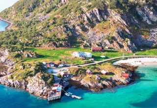 Vista aerea di Engvik Hytta, cabine sul mare, acque turchesi, spiaggia e colline verdi nella natura svedese.