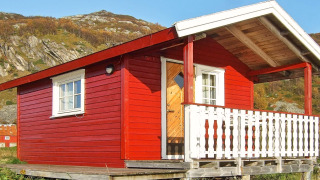 Casetta rossa chiamata ENGVIK HYTTA 83699 con veranda bianca, situata su palafitte in un paesaggio collinare.
