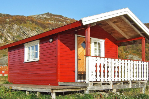 Casetta rossa chiamata ENGVIK HYTTA 83699 con veranda bianca, situata su palafitte in un paesaggio collinare.