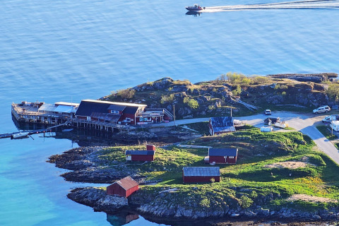 Vista costiera da Engvik Hytta 83699 in Svezia con casette rosse, molo e una barca sull’acqua tranquilla.