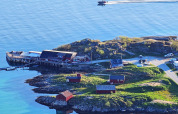 Vista costera desde Engvik Hytta 83699 en Suecia, con cabañas rojas, muelle y bote sobre aguas tranquilas.