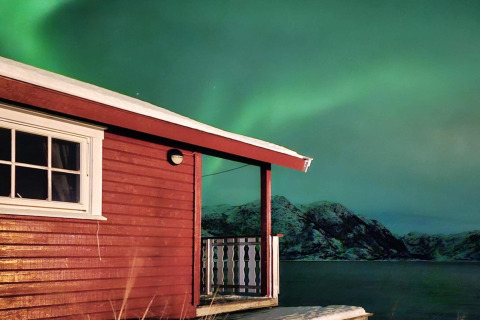Baita rossa col tetto innevato vicino al lago e aurora boreale, Engvik Hytta, Svezia.