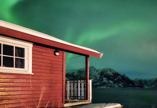 Baita rossa col tetto innevato vicino al lago e aurora boreale, Engvik Hytta, Svezia.