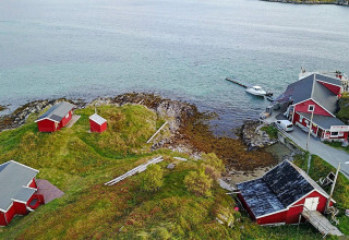 Vista aerea di cabine rosse sull’acqua con un pontile, circondate da colline verdi in Svezia.