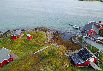 Foto aérea de cabañas rojas junto al agua y un muelle, rodeadas de colinas verdes en Suecia.