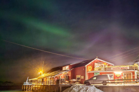 Foto di notte di Engvik Hytta 83699 in Svezia, con aurora boreale e una cabina innevata illuminata.