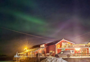 Foto nocturna de Engvik Hytta 83699 en Suecia, luces del norte sobre una cabaña nevada y luces cálidas.