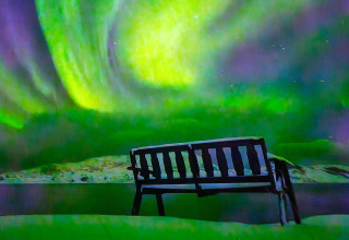Una panchina innevata guarda l'aurora boreale da ENGVIK HYTTA 83699 in Svezia.