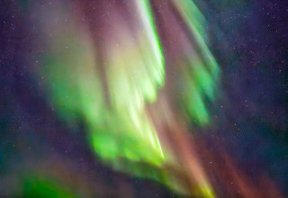 Aurora boreale con sfumature verdi e viola, vista dalla cabina ENGVIK HYTTA 83699 sotto il cielo notturno svedese.