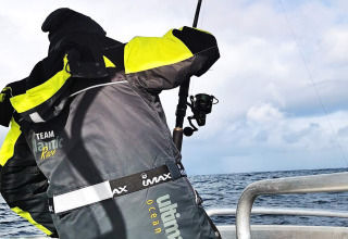 Persona con giacca 'TEAM Atlantic Race' che pesca da una barca vicino a ENGVIK HYTTA 83699 in Svezia.