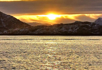 Atardecer desde Engvik Hytta 83699, Suecia, con montañas nevadas y lago resplandeciente en primer plano.
