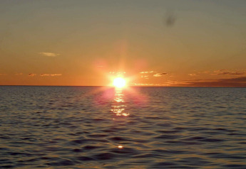 Zonsondergang boven zee bij ENGVIK HYTTA 83699 in Zweden, met kalme golven en een oranje gekleurde lucht.