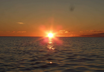 Vista de la puesta de sol sobre el mar desde ENGVIK HYTTA 83699 en Suecia, con agua tranquila y cielo naranja.