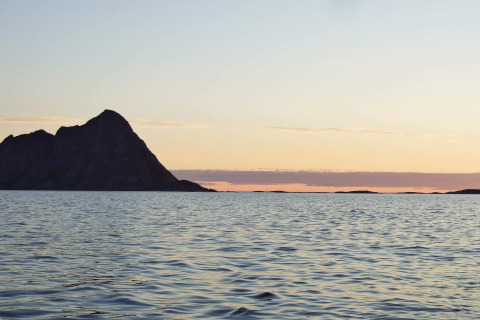 Tramonto visto da ENGVIK HYTTA 83699 in Svezia, mare calmo e un’isola scura all’orizzonte all’imbrunire.