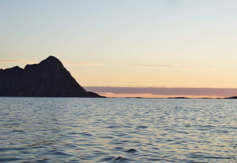 Vista del atardecer desde ENGVIK HYTTA 83699 en Suecia, con mar tranquilo y una isla silueteada al fondo.