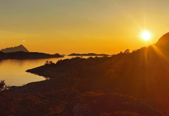Atardecer sobre montañas y agua desde Engvik Hytta 83699 en Suecia, con luz dorada en el paisaje.