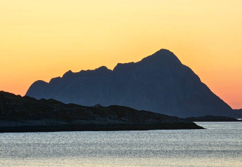 Atardecer sobre montañas y lago, visto desde ENGVIK HYTTA 83699 en Suecia, con siluetas oscuras y cielo naranja.