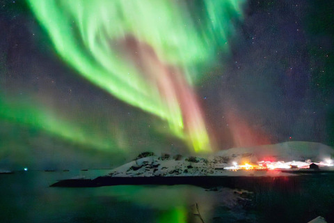 L'aurora boreale sopra un'isola innevata e una baita illuminata a Engvik Hytta 83699, in Svezia.